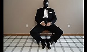 Seated in a tuxedo wearing a rubber cock and ball sheath and playing with my cock until I cum.